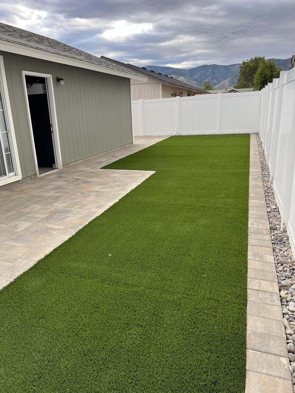 Narrow side yard laid with artificial turf against a white vinyl fence